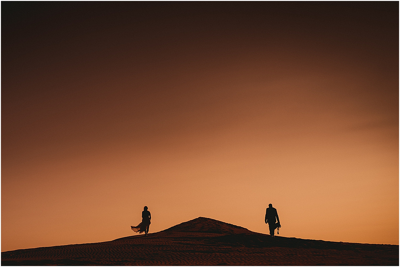 Wedding couple climbing a sand dune at sunset